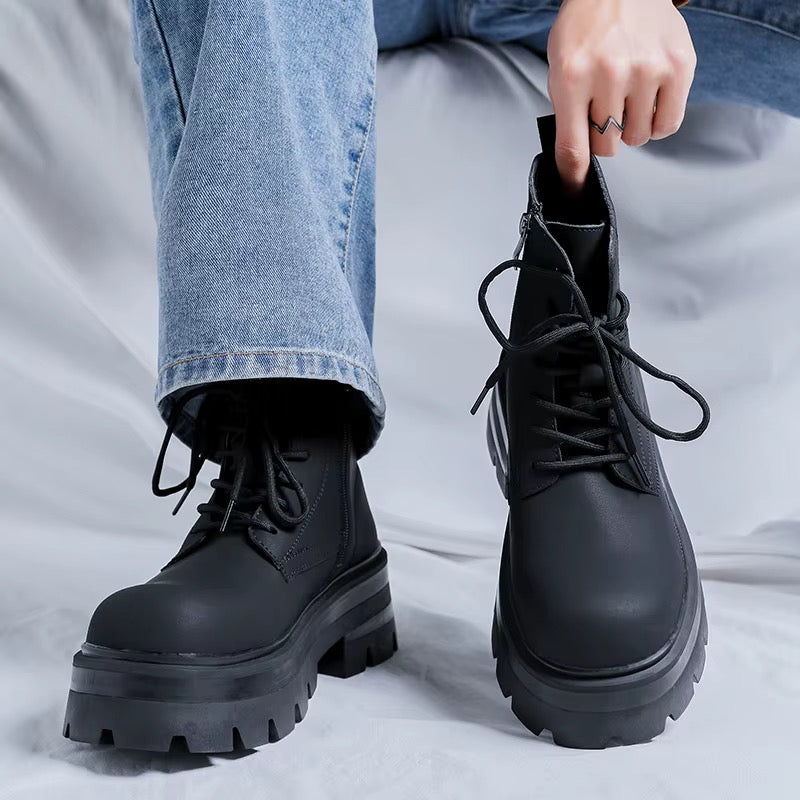Vue de face de bottines noires à plateforme pour homme, portées avec un jean bleu, lacets noirs et semelles épaisses crantées.