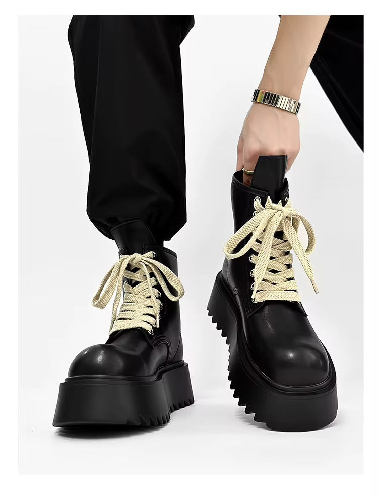 Vue de face de bottines noires à plateforme pour homme, portées avec un pantalon noir, lacets crème et semelles épaisses crantées.