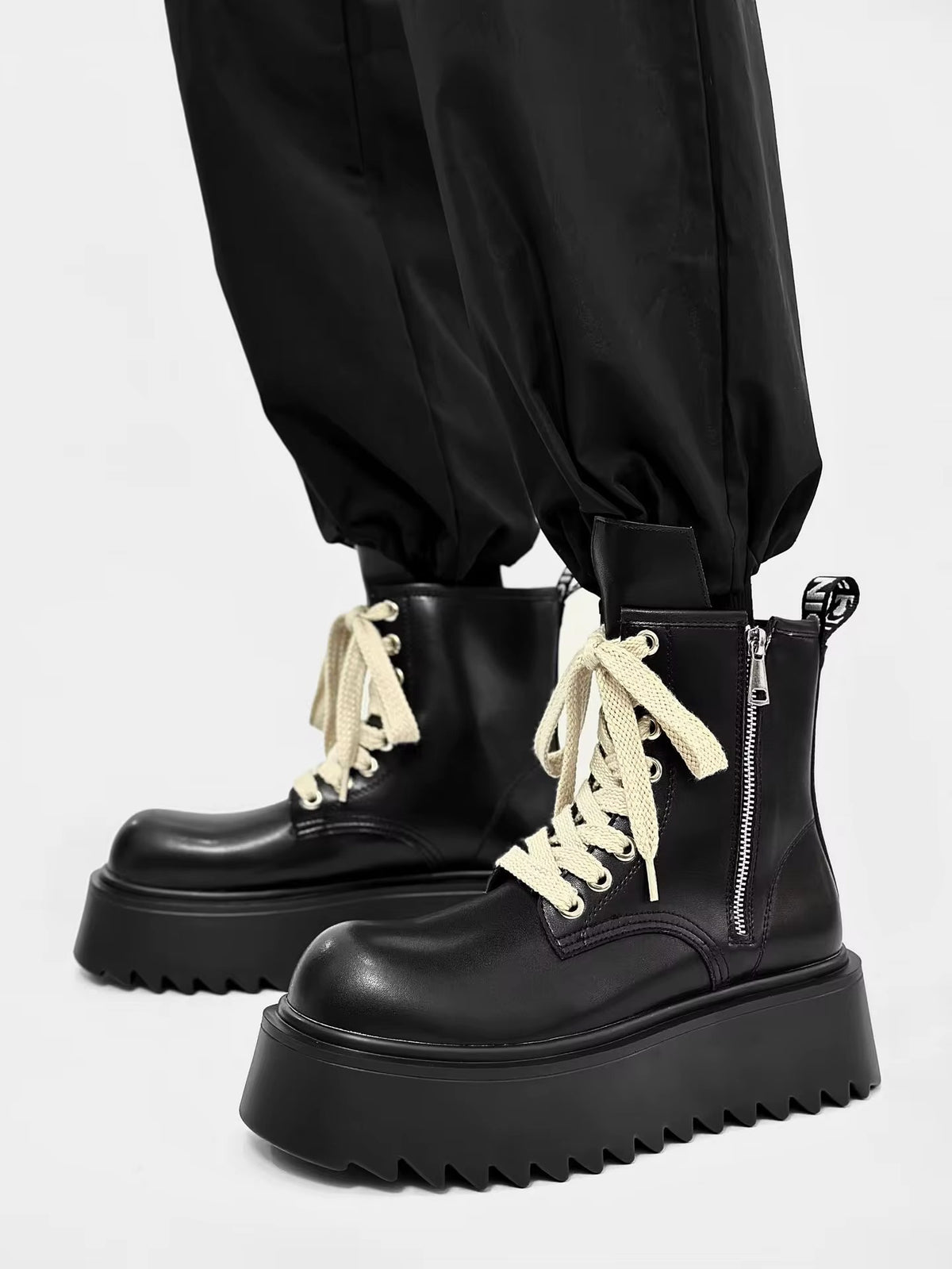 Bottines noires à plateforme pour homme, vue de trois quarts avec lacets crème, fermeture éclair latérale et semelle épaisse crantée.